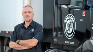 A man poses with his arms crossed in front of a Spee Dee Delivery truck